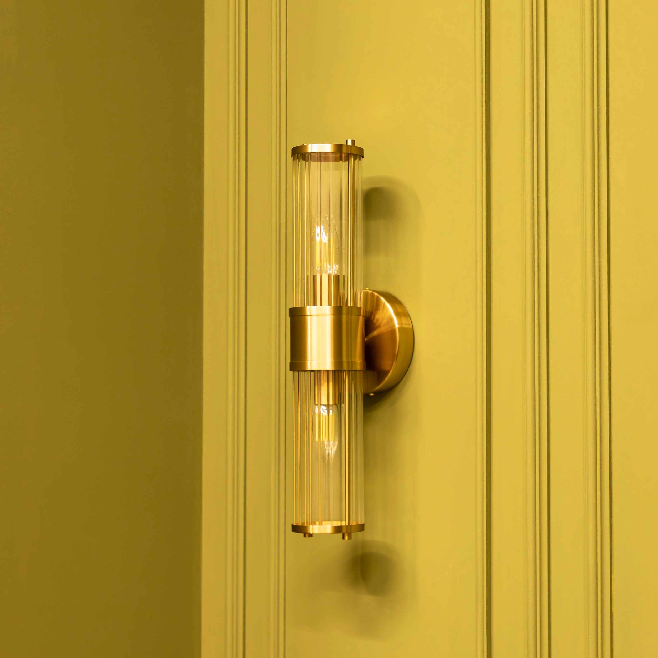 Gold wall sconce with clear glass shade on a yellow wall
