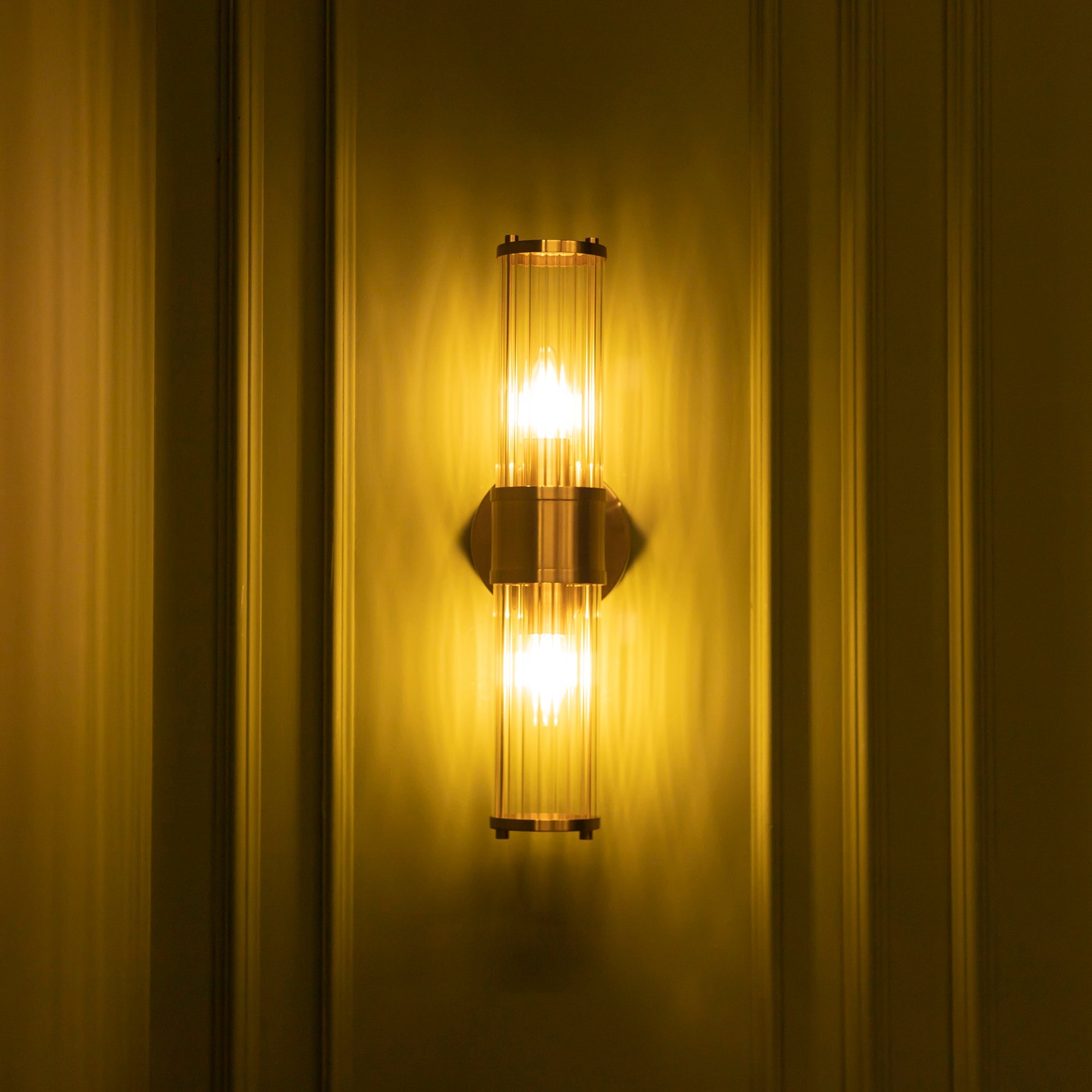 Wall-mounted light fixture with a warm glow on a yellow wall.