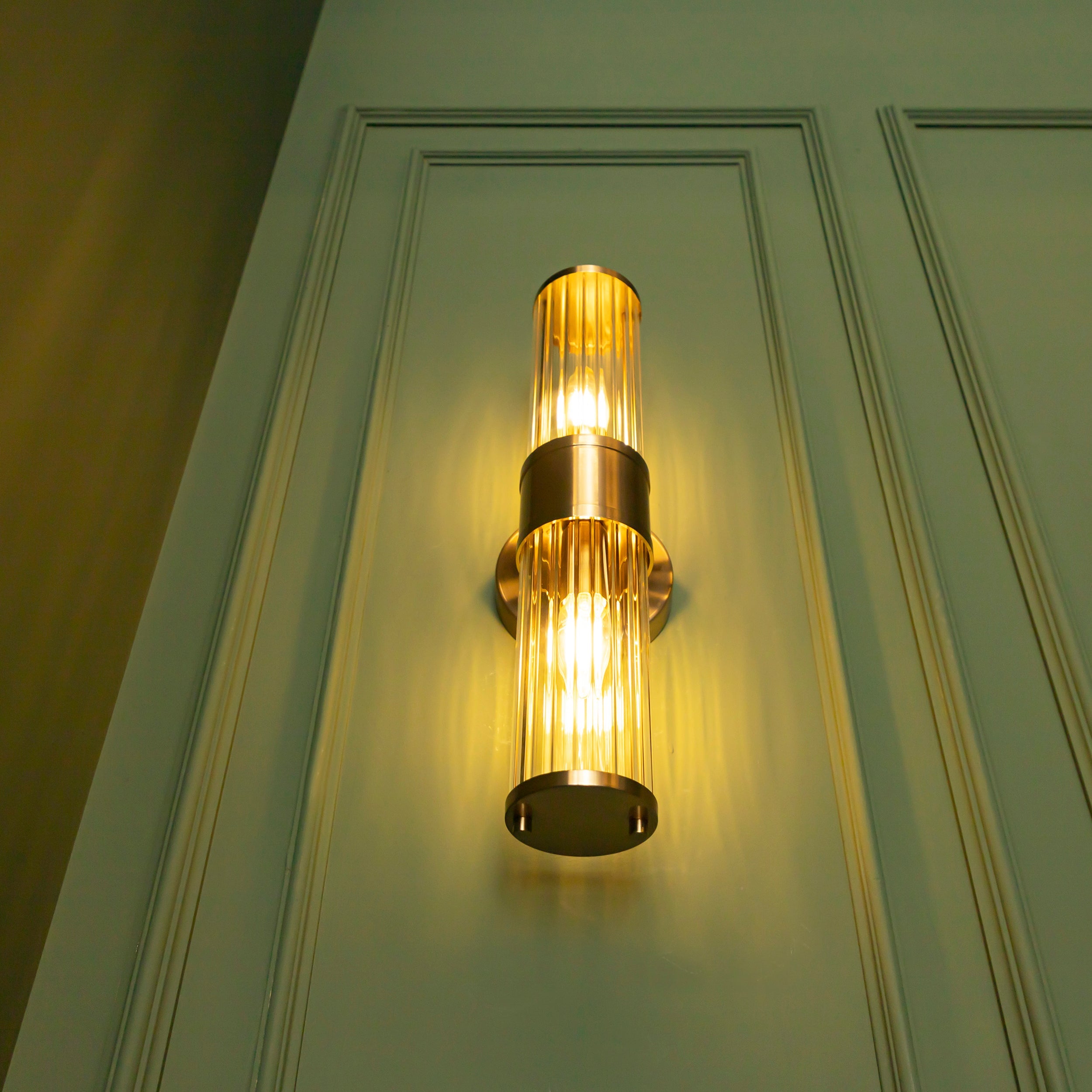 Gold wall sconce with clear glass shade on a green door