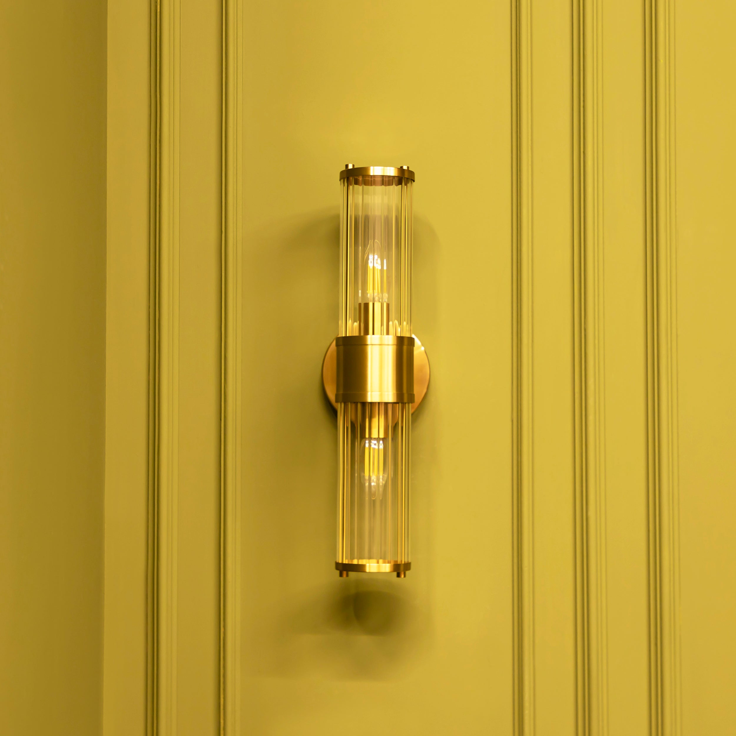 Gold wall sconce with clear glass shade on a yellow-painted wall