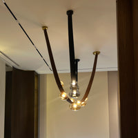 Modern chandelier with glass bulbs hanging from black metal rods against a neutral wall.