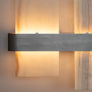 A modern wall sconce featuring a brushed metal horizontal bar mounted on vertical textured stone panels that glow with warm light.