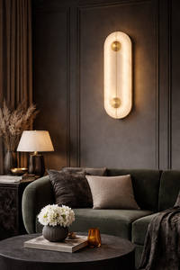 Glowing oval alabaster wall sconce with gold accents mounted in a dark elegant living room